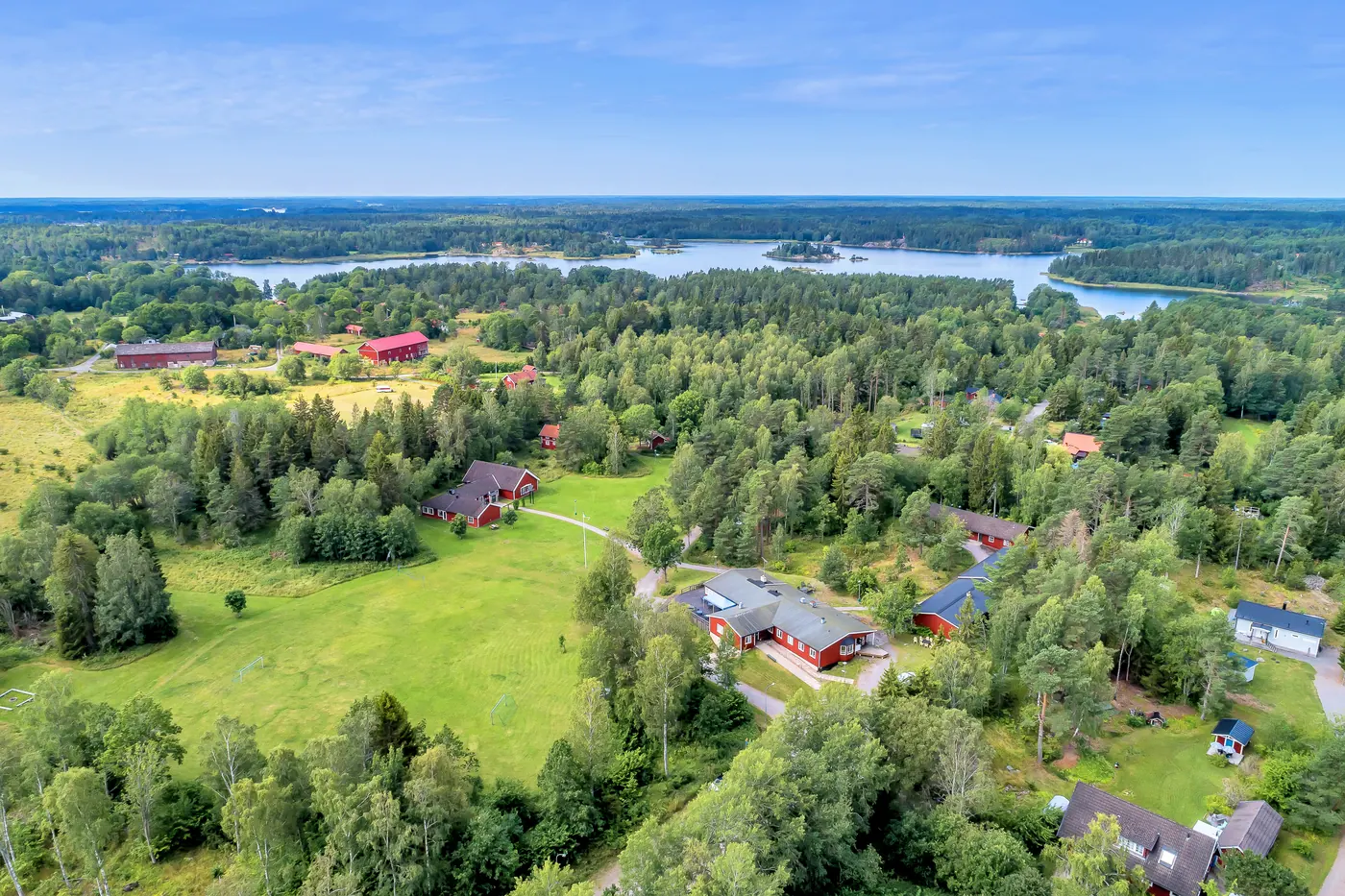 Flygbild över gården och skogen, med skärgårdens vatten i bakgrunden